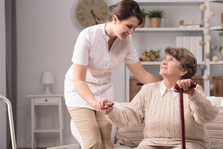 Young,Carer,Supporting,Senior,Disabled,Woman,With,Walking,Stick.