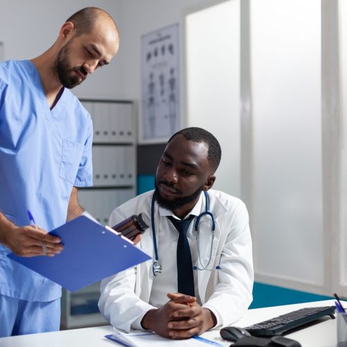 Medical team of practitioners analyzing disease symptoms discussing healthcare treatment working in hospital office. Doctor checking medicine prescription during clinical appointment