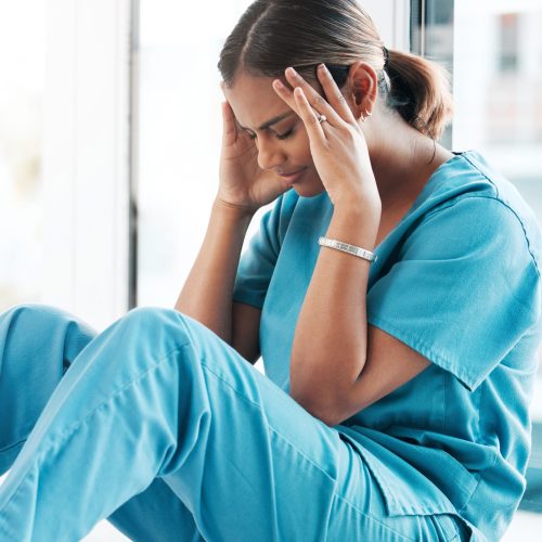 Depression, headache and medical with nurse on floor of hospital for sad, mental health and burnout.