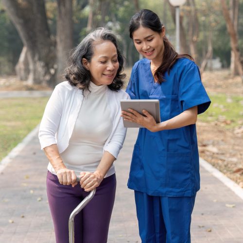 nurse caregiver showing a tablet screen to senior woman and laughing at walking in park for healthcare or nursing home nurse caregiver showing a tablet screen to senior woman and laughing at walking in park for healthcare or nursing home.