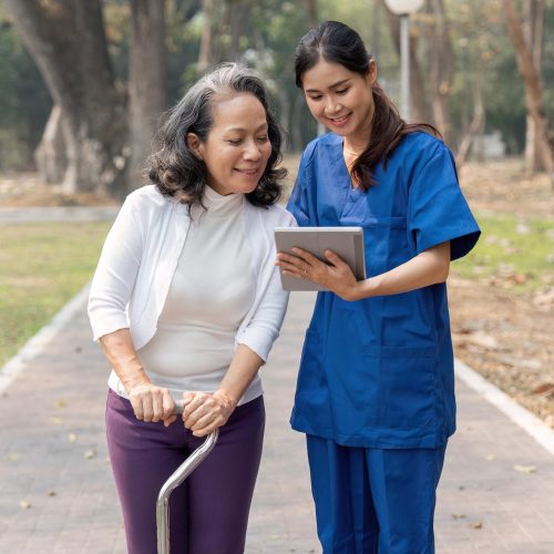 nurse caregiver showing a tablet screen to senior woman and laughing at walking in park for healthcare or nursing home.