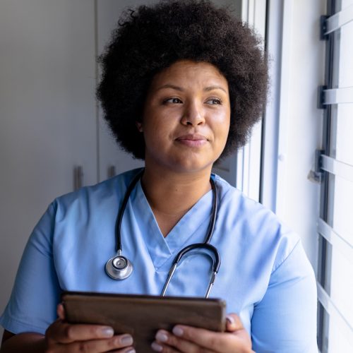 Smiling african american mid adult female nurse looking away while holding digital tablet. unaltered, healthcare worker, expertise, wireless technology and occupation concept.