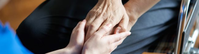 Hands of elderly people in wheelchairs and caregivers